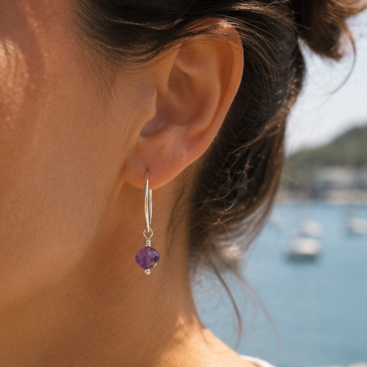 Sterling silver hoop earring with amethyst gemstone dangling on lady with coastal background 