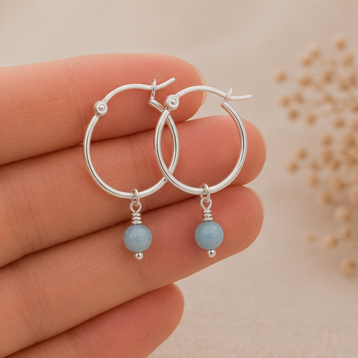 Female fingers holding a pair of hoop earrings with aquamarine gemstone dangling off