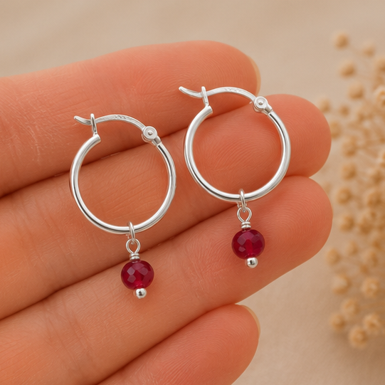 Sterling silver hoops laid on top of fingers with Ruby gemstone dangle.